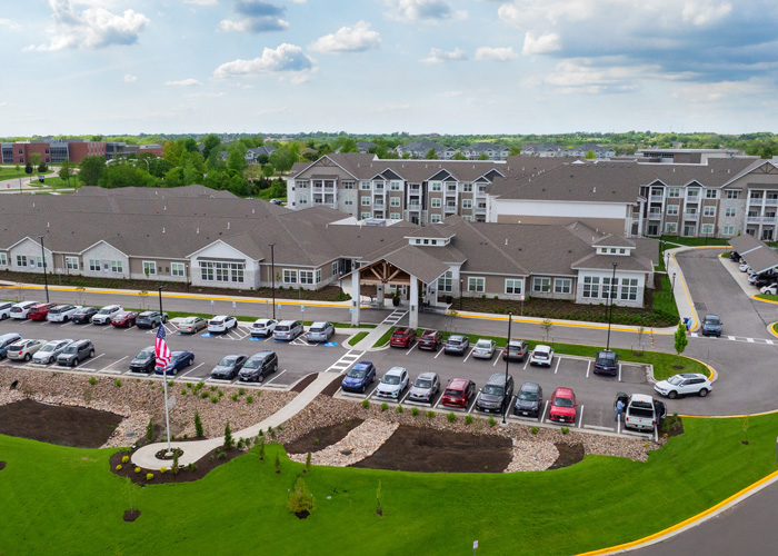 Aerial view of The Crestone Senior Living community showing its expansive layout, modern design, parking lot with cars, and surrounding greenery.