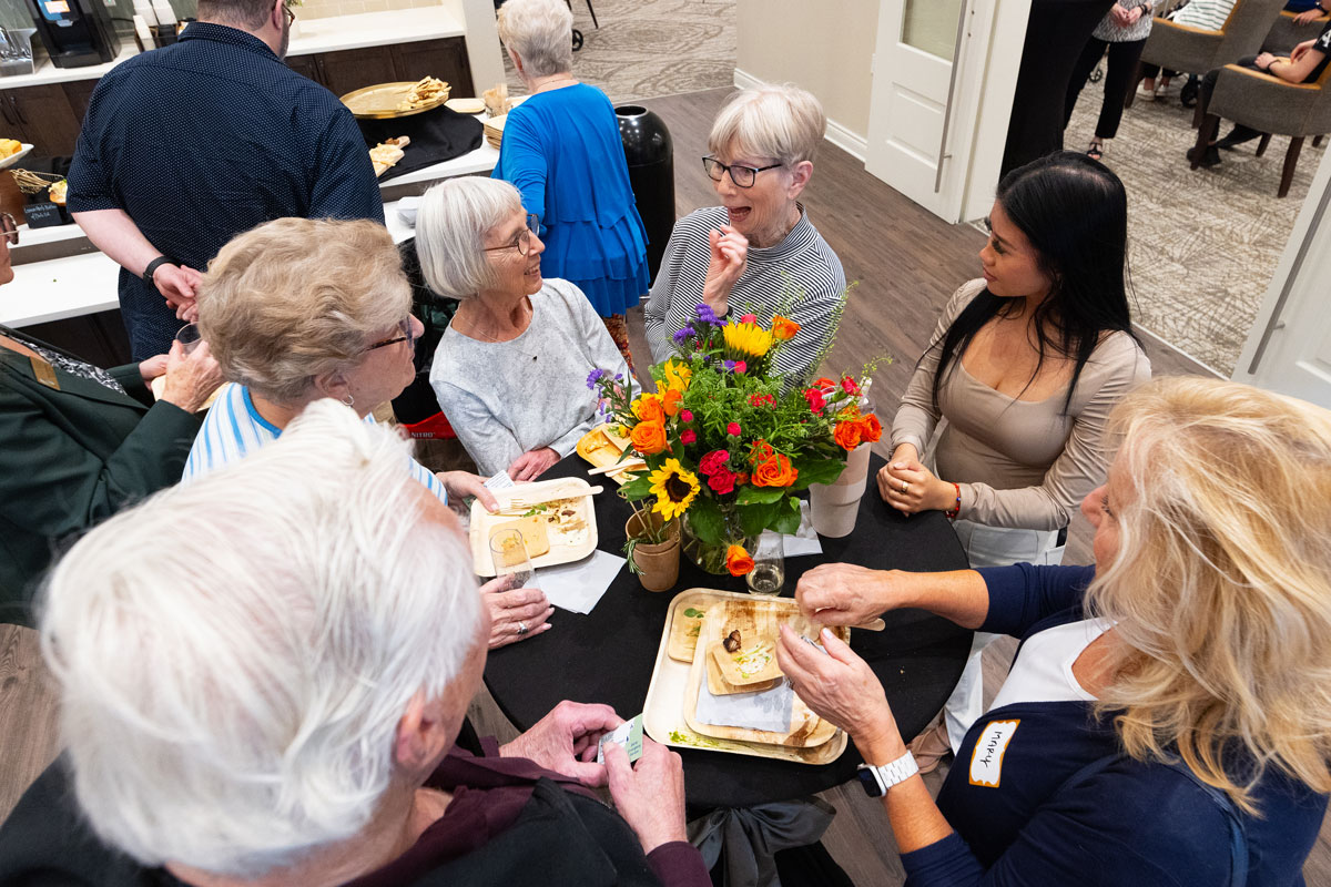Residents and guests gather around a table indoors at The Crestone Senior Living, enjoying appetizers and conversation during the grand opening celebration.