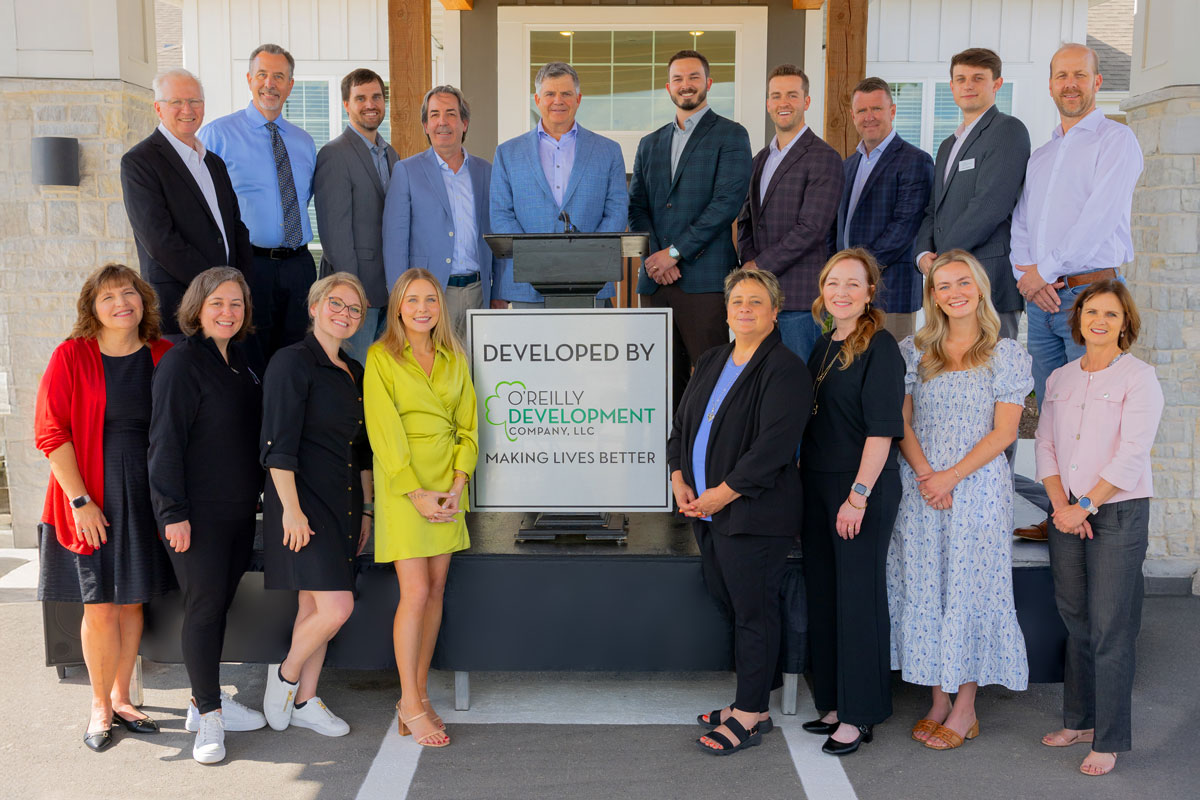 A large group of people stands outside The Crestone Senior Living entryway, posing around a podium and sign that reads “Developed by O’Reilly Development Company, LLC.”