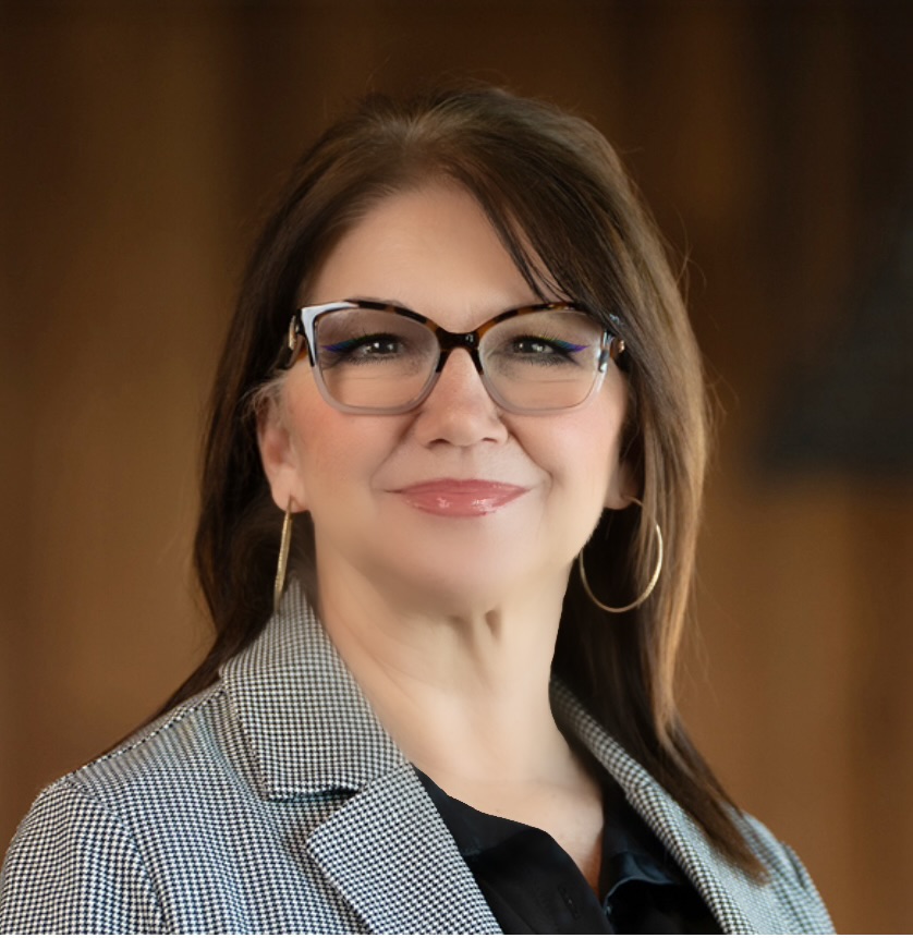 Candace Starr, Resident Services Director at The Crestone, wearing glasses and a checkered blazer over a black blouse, smiling confidently against a softly lit background.
