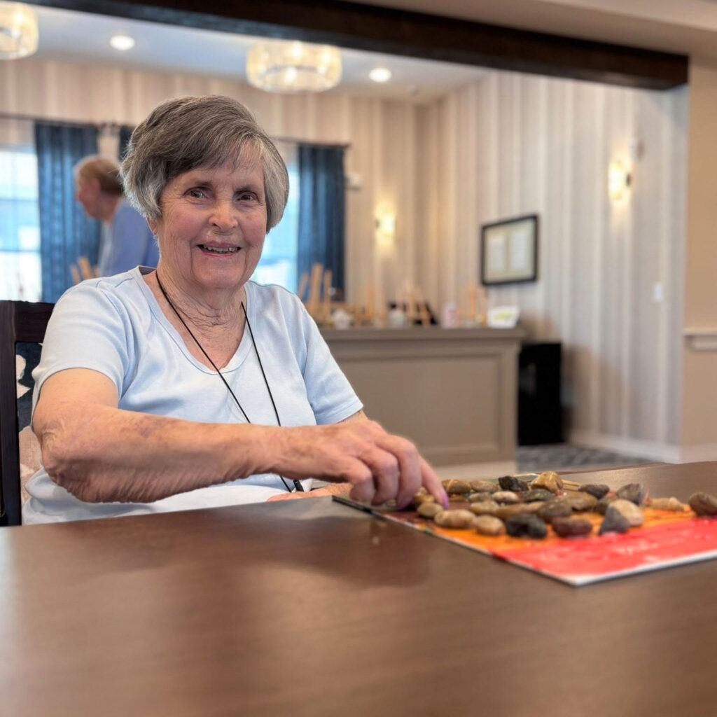 A cheerful resident smiles while arranging stones on a colorful board during a hands-on activity, enjoying creativity and engagement in the community.