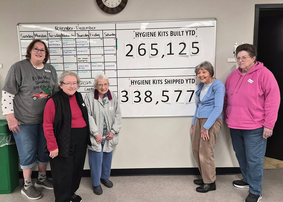 Senior residents proudly posing next to a white board displaying "Hygiene Kits built year to date: 265,125".