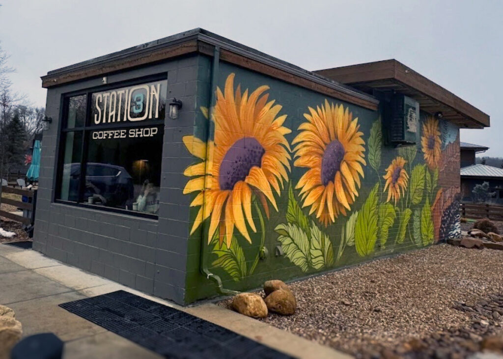 The exterior of Station 3 Coffee Shop, the side painted in a colorful mural of realistic yellow flowers.