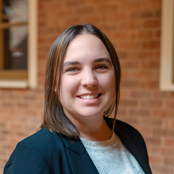 Dee Morse, Wellness Director at The Crestone Senior Living, smiling in a professional outdoor headshot with shoulder-length dark hair, a black blazer, a light textured top, and a softly blurred brick background.