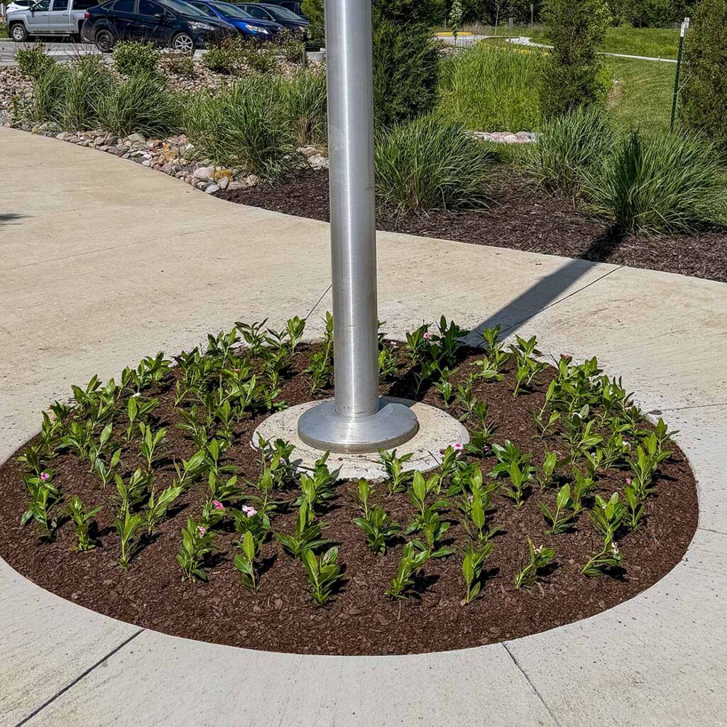 A landscaped flag pole featuring just-planted flowers.